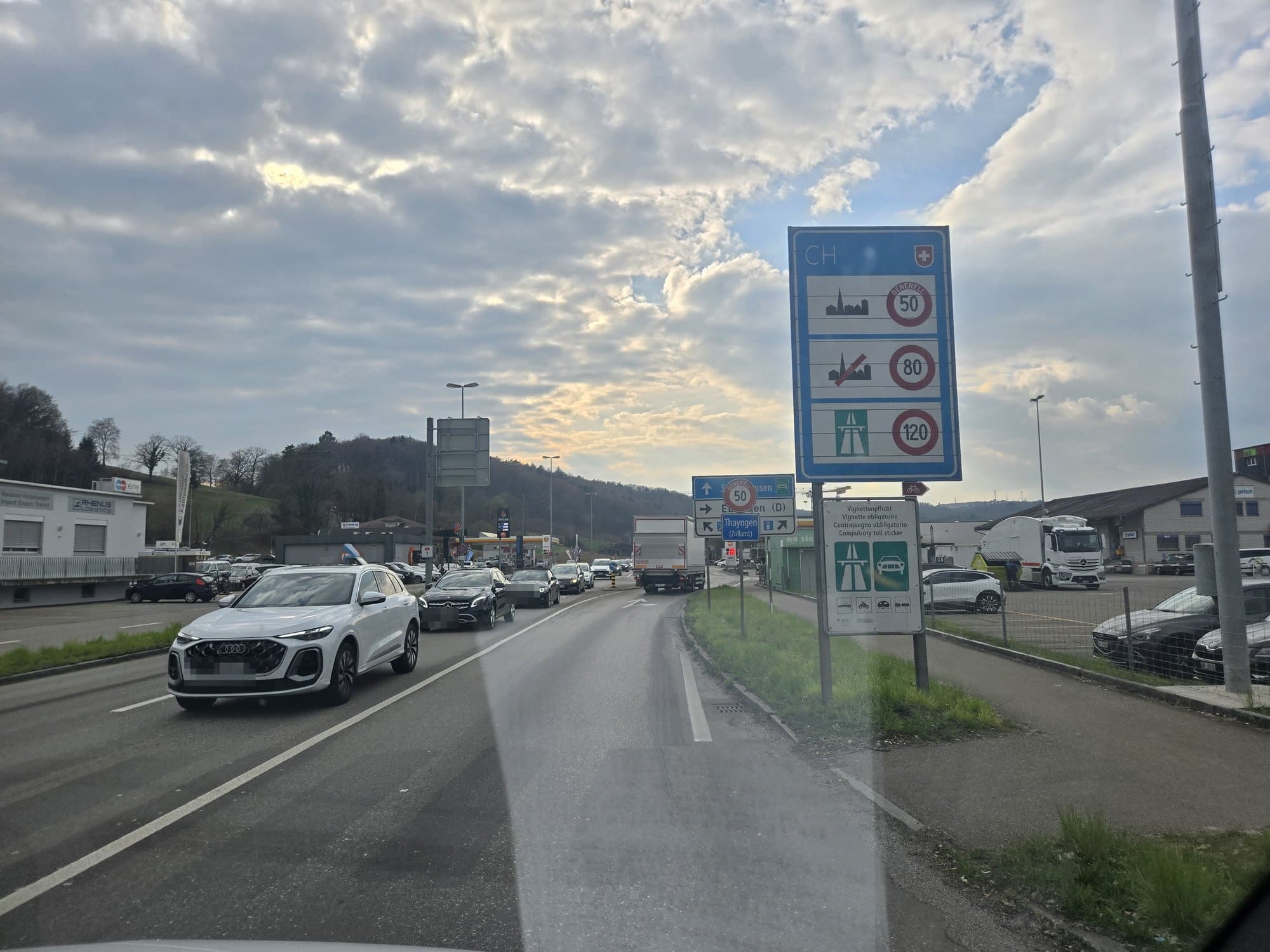 Grenzübergang in die Schweiz mit Zollschild, Tempolimits und Vignettenpflicht, davor wartende Fahrzeuge