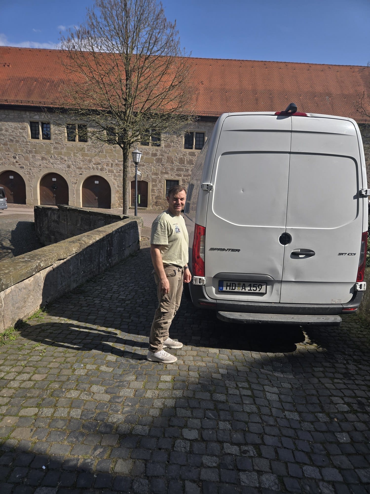 Stefan Arndt von Umzugflex24 steht neben dem Sprinter vor einem historischen Gebäude in der Schweiz