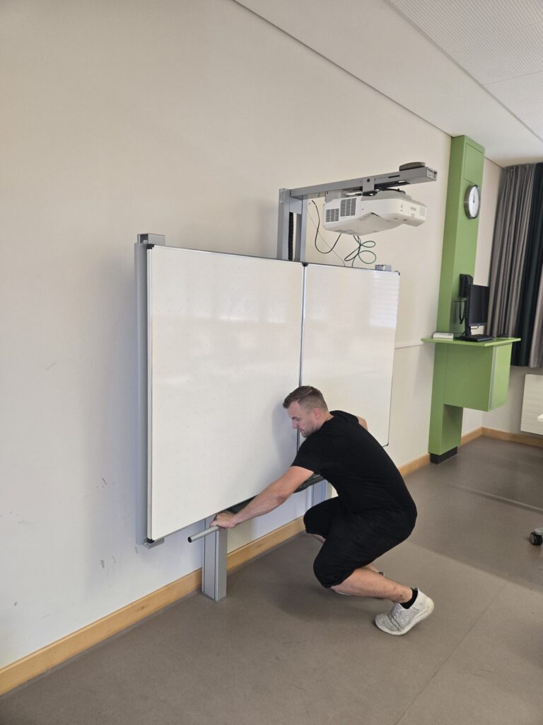 Pylonentafel mit Kurzdistanzbeamer an der Deckenschiene in einem Klassenzimmer, Monteur beginnt mit der Demontage