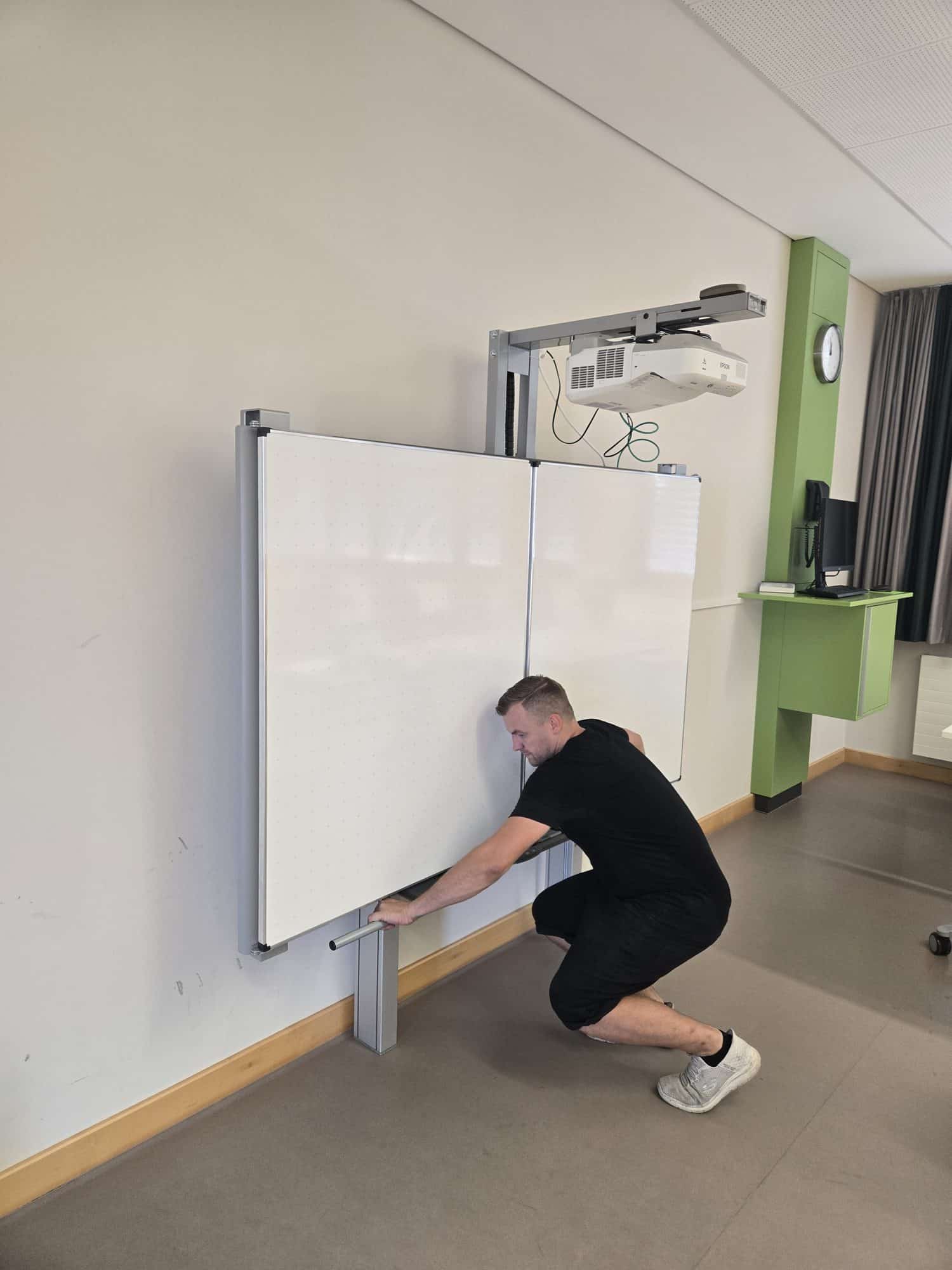 Pylonentafel mit Kurzdistanzbeamer an der Deckenschiene in einem Klassenzimmer, Monteur beginnt mit der Demontage