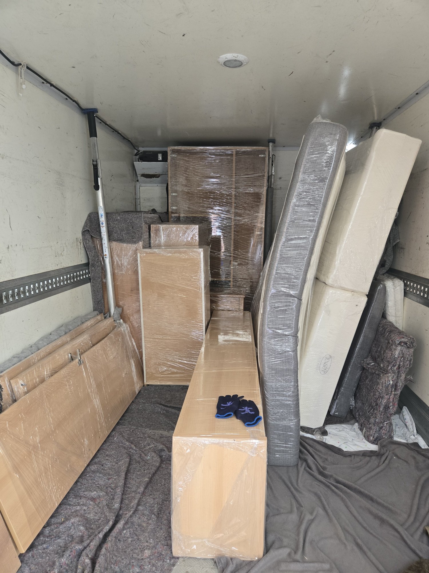 Beladener Umzugswagen mit in Folie verpackten Möbeln, Matratzen und Decken zur Sicherung